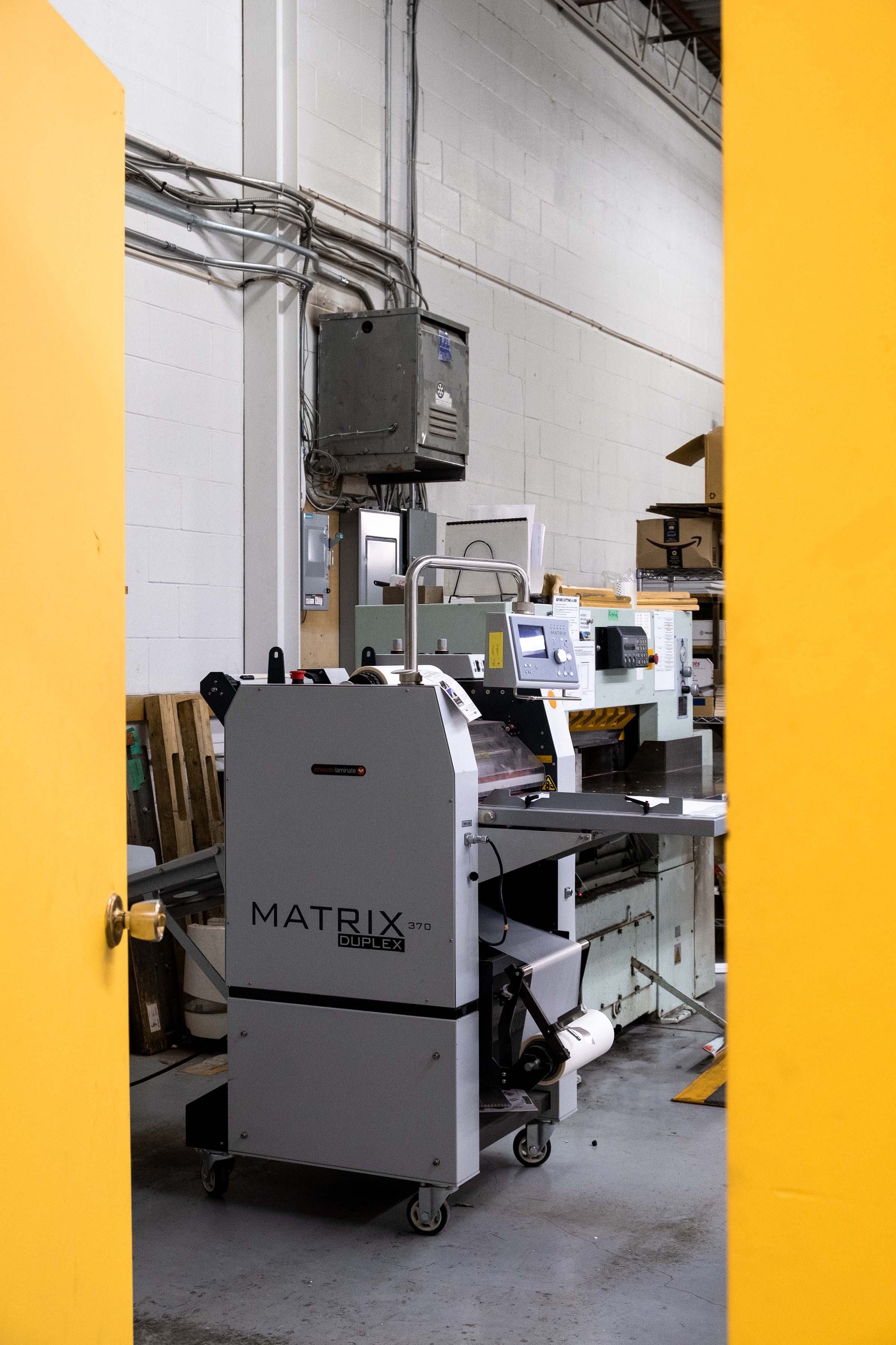 A Matrix 370 laminator framed by yellow doors in the Outside the Box print shop.